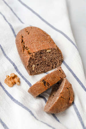 Delicious freshly baked bread with walnuts on white kitchen towel, vertical image