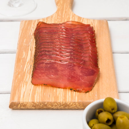 Cutting board with sliced dry salami on white table and olivesの写真素材