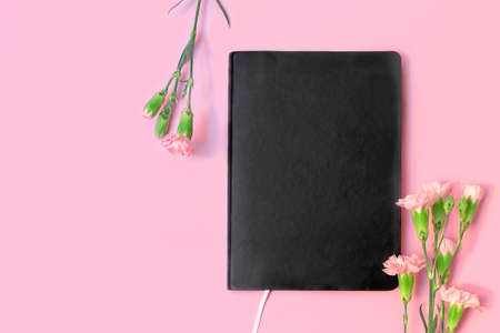 Top view of black empty book or notebook and flowers on pastel pink background with copy space.の写真素材