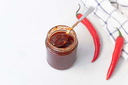 Above view of jar with sweet spicy jam made from chili pepper on neutral grey background with copy space, selective focus