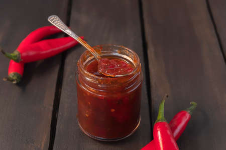 Glass jar of spicy chili jam with red peppers on wooden backgroundの写真素材