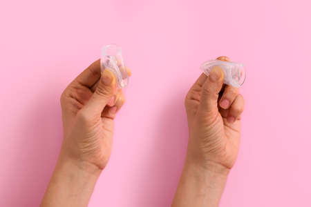 Womans hand showing two ways of folding menstrual cup on pastel pink background with space for text