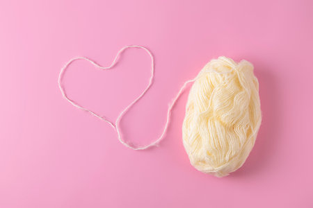 Top view of heart made from a woolen thread with ball of yarn on light pink backgroundの写真素材