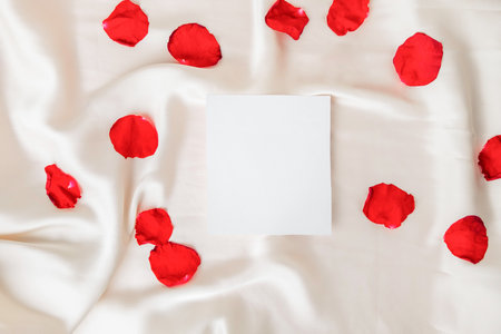 Romantic backdrop with satin fabric, rose petals and empty white paper for copy space. Note on a bed conceptの写真素材