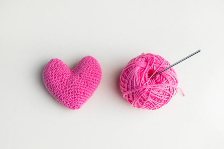 Crochet pink heart, ball of yarn and a crochet hook on light background, top viewの写真素材