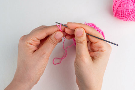 Hand holding thread of pink yarn and a chrocket hook on light background. Tutorial on how to crochet...