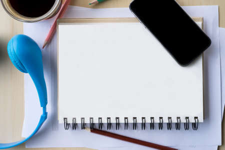 top view blank screen of mobile phone on notebook and wooden desk with pencil and headphoneの写真素材