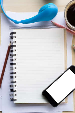 top view blank screen of mobile phone on notebook and wooden desk with pencil and headphoneの写真素材