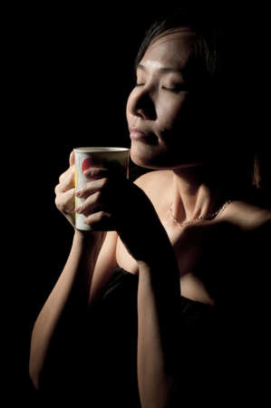 Attractive woman  with an aromatic coffee in hands isolated on black backgroundの写真素材