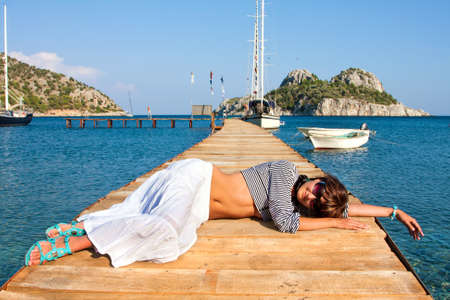 Happy young woman on holidays on the sea, lie on a bridgeの写真素材