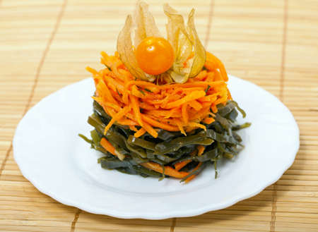 Appetizing of carrot and laminaria on a white plate and bamboo servietteの写真素材