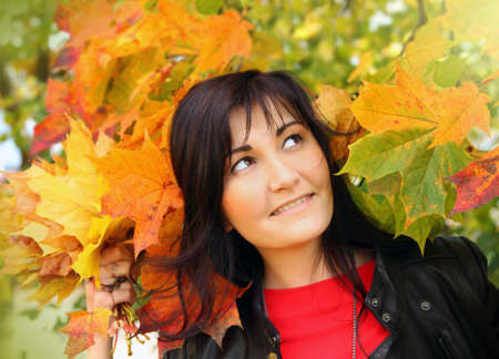 Beautiful young woman with maple leaves in autumn park