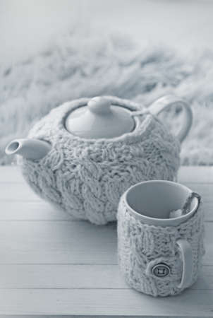 Teapot and cups in knitted clothes on a tray in winter evening on kitchenの写真素材
