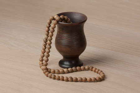 Clay jug with wooden beads on a wooden tableの写真素材