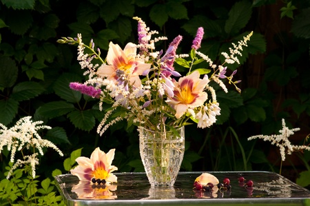 still life bouquet with hemerocallis, astilba and hosta with black currants on the table in a dark green leaves backgroundの写真素材
