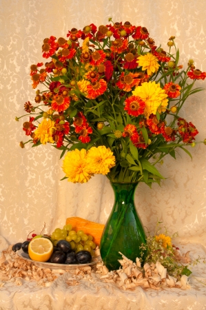 still life with bright yellow and orange flowers in the green vase with fruitsの写真素材