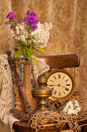 still life with phlox bouquet in a vintage vase on the old chair with antique clock and oil lampの写真素材