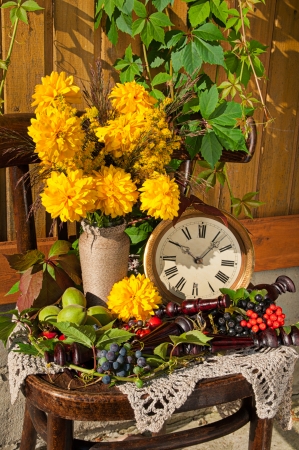 golden sphere yellow flowers bouquet in the old wooden chair with antique clock in a sunny day still lifeの写真素材