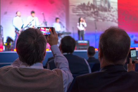 people sitting rear holding their mobile phones and making video record of the concert