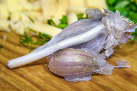garlic laying on a wooden table and sliced cheese and dill on the backの写真素材