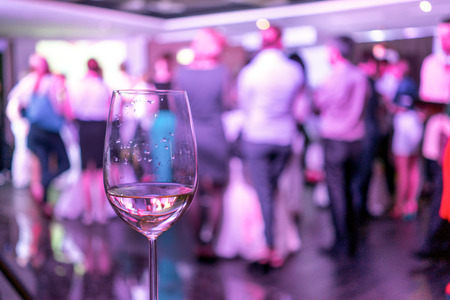 blurred image from a crowd of people standing in a party and a glass of white wine on the front...