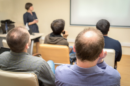 Back view of an adult students audience listening the presentation of a woman teacher near the screenの写真素材