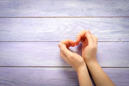 Woman hands making a heart shape on a wooden background with copy spaceの写真素材