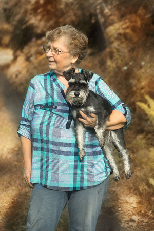 elderly woman standing on the background of autumn nature with a dog miniature schnauzer on hands