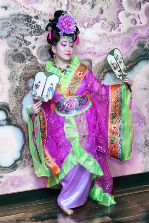 Portrait of young Chinese female in traditional dress with fans, full length against marble wall background.の写真素材