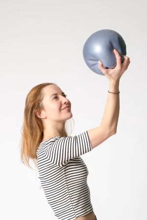 Slim smiling fitness young girl holds blue ball on her hand extended upwards and looking at it. Studio shot.の写真素材