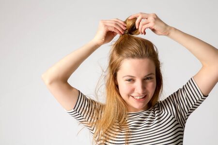beautiful young caucasian woman corrects her hair, studio shot, grey background, copy space.