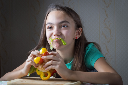 11 year old girl eating a hamburger, mouth sticks lettuce leaf as a mustacheの写真素材