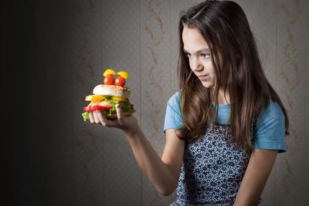 11 year old girl holding at arm hamburger decorated as smiley face with eyes of cherry tomatoes, and looks at it.の写真素材