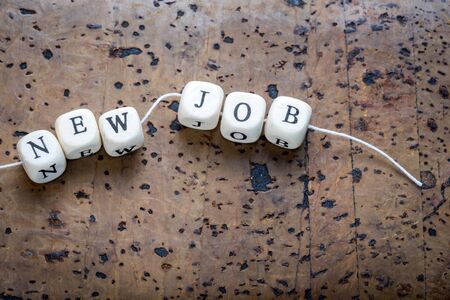 New job text on a wooden cubes strung on a thread on a brown cork backgroundの写真素材