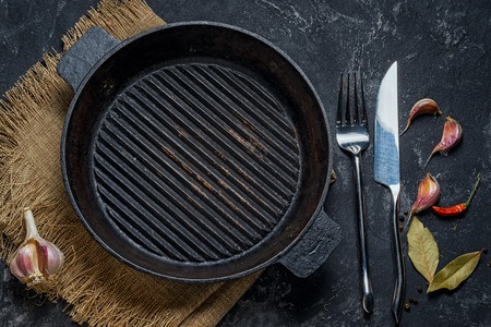 Black iron empty grill pan, seasonings, fork and knife on cement black texture backgroundの写真素材