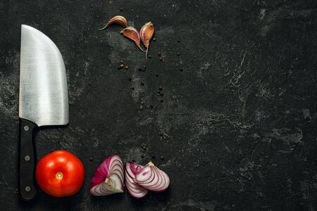 food background. dark black cement background and knife, tomatoes, garlic, onion and pepper with plenty of copy space for your inscription.の写真素材