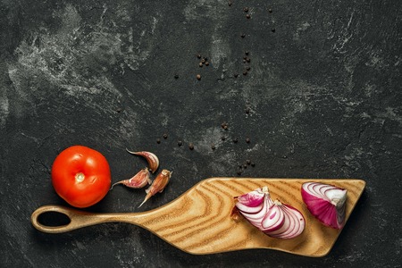 dark food background with cutting board, tomatoes, garlic and onion at the bottom, and copy space at the top for your inscriptionの写真素材
