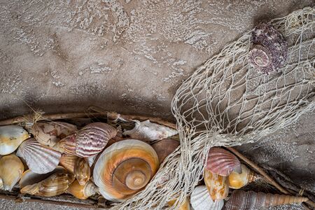 holiday background, seashells stacked in the shape of a boat and fishing net on a beige background...