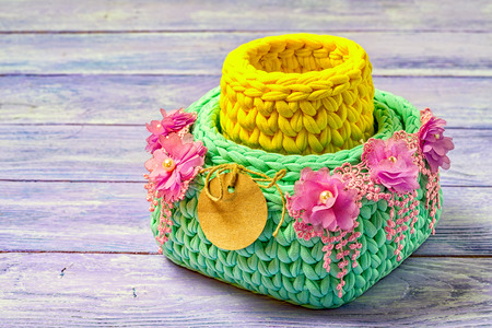Knitted baskets decorated with lace flowers, with a blank circular paper label. copy space on a wooden background.の写真素材
