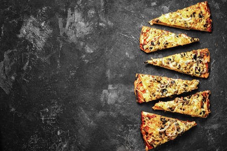 pizza pieces lying on the faded textural dark black background in a row, copy space for your menu...