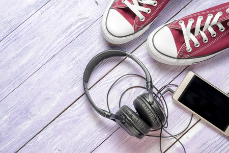 gumshoes, cell phone and headphones on a wooden background, top view, copy space