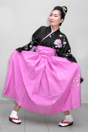 A funny geisha in a kimono fools around, lifting her skirt and clapping her feet.の写真素材