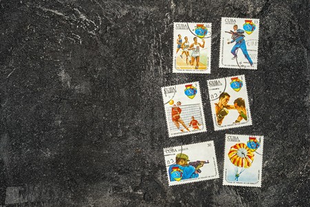 Moscow, Russia - April 20, 2017: set of randomly lying postage stamps printed in Cuba shows athletes and various sports, devoted to 4 Spartakiad,  series, circa 1977, on a dark black cement backgroundのeditorial素材