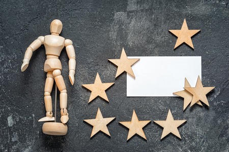 business conceptual still life with mannequin, blank business card with copy space, and group of wooden stars on a dark cement background, top view.の写真素材