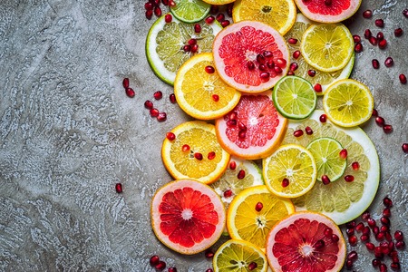 border frame from citrus slices with pomegranate seeds, top view on a rustic beige cement background with copy spaceの写真素材