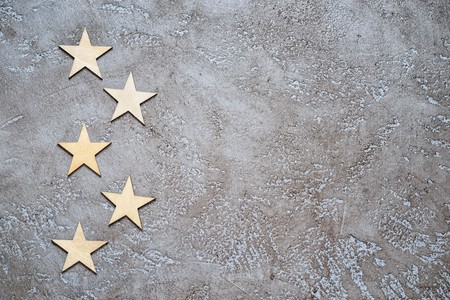 five wooden stars lie zigzag in the form of bullets on the left of a textured neutral cement background with copy space for your text.の写真素材
