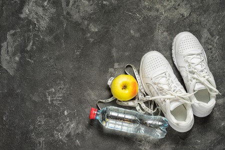 sports background top view of sneakers, bottle of water, apple and sentimeter tape on a black background with copy space.の写真素材