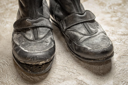Warn out old black leather boots close up on the beige cement backgroundの写真素材