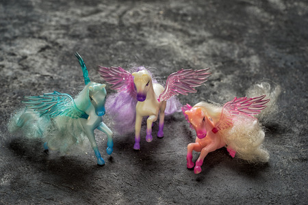 three pegasus horse toys on a black cement background, side view with copy spaceの写真素材