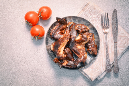 delicious smoked chicken wings on plate and tomatoes, served with fork and knife, top view. copy...